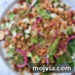 A vibrant Blackened Chicken Salad with greens, quinoa, chickpeas, sliced almonds, carrots, and pickled onions on a plate, ready to be enjoyed with a fork.