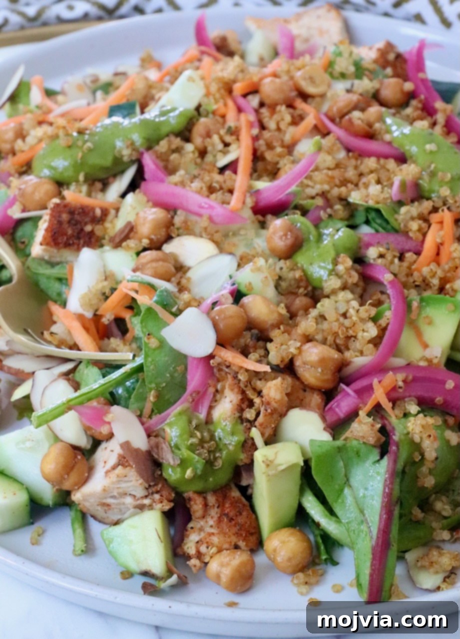 Bayou Blackened Chicken Salad 10 A vibrant, fully assembled Blackened Chicken Salad featuring greens, crispy quinoa, savory chickpeas, crunchy sliced almonds, fresh carrots, and tangy pickled onions, presented on a plate.