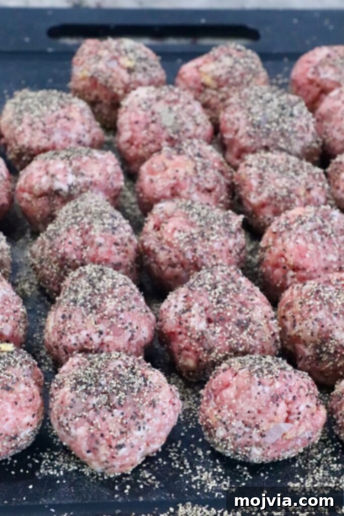 Creamy Peppercorn Meatballs 5 raw meatballs covered in black pepper on a dark cutting board