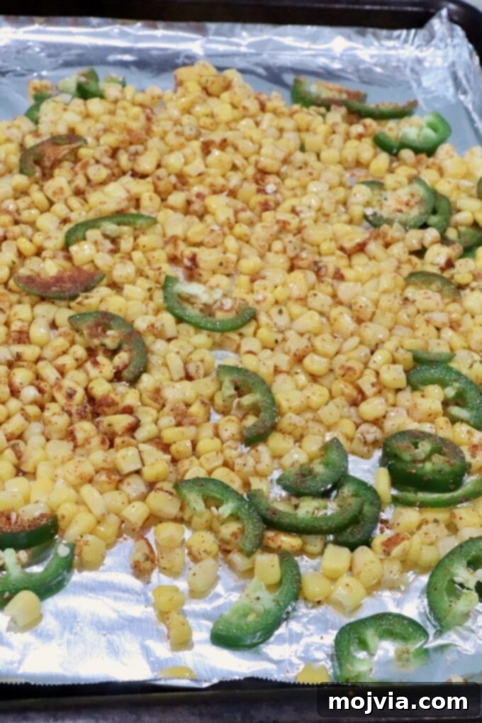 seasoned corn kernels and sliced jalapenos on a foil-lined baking sheet