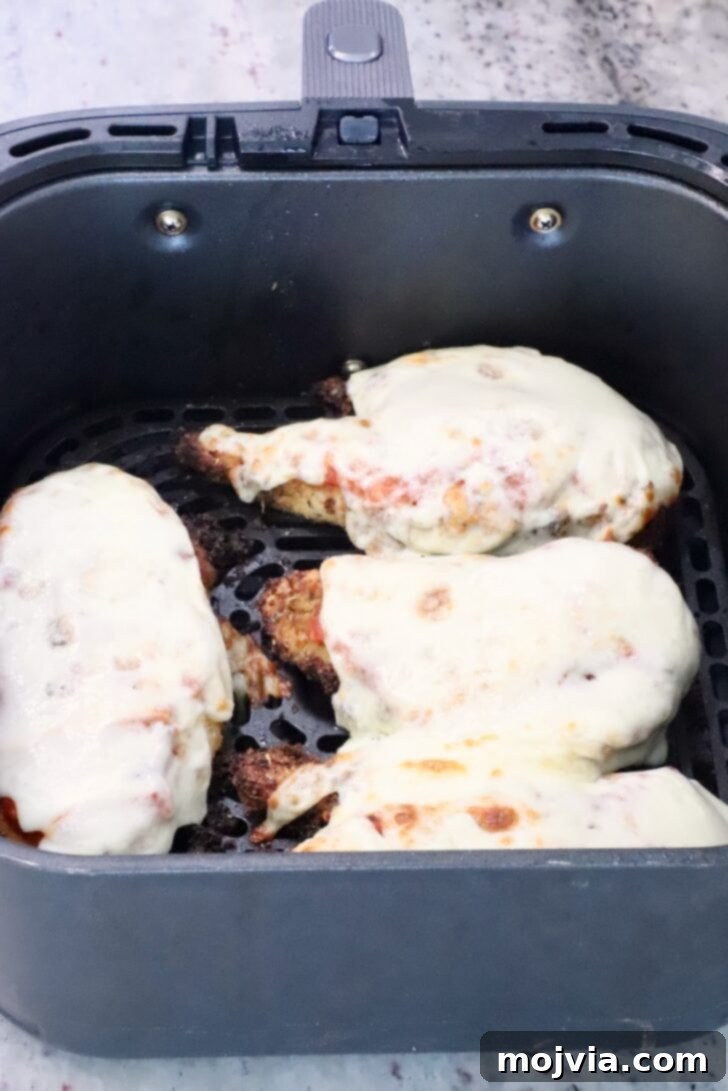 The Ultimate Air Fryer Chicken Parmesan 11 Four perfectly cooked Air Fryer Chicken Parmesan pieces with melted mozzarella, glistening in the air fryer basket, ready to be removed.