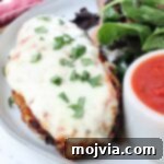 The Ultimate Air Fryer Chicken Parmesan 13 Air Fryer Chicken Parmesan with melted mozzarella, garnished with fresh basil, served on a plate with a side salad and a small bowl of marinara sauce.