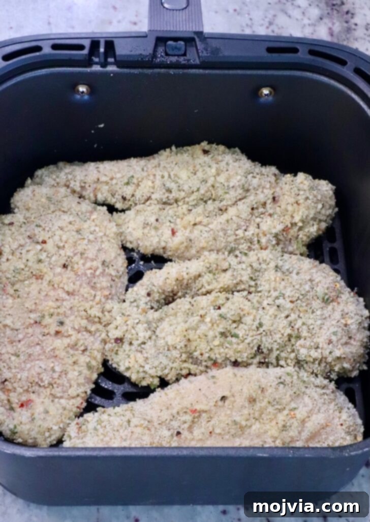 The Ultimate Air Fryer Chicken Parmesan 7 Two breaded chicken breasts carefully placed in an air fryer basket, showing space for air circulation.