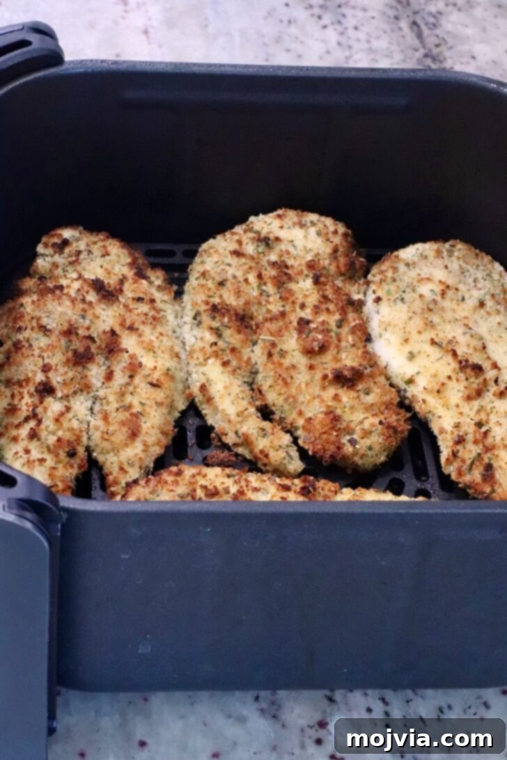 The Ultimate Air Fryer Chicken Parmesan 8 Air-fried chicken breasts, golden and crispy, shown inside the air fryer basket after the initial cooking phase.