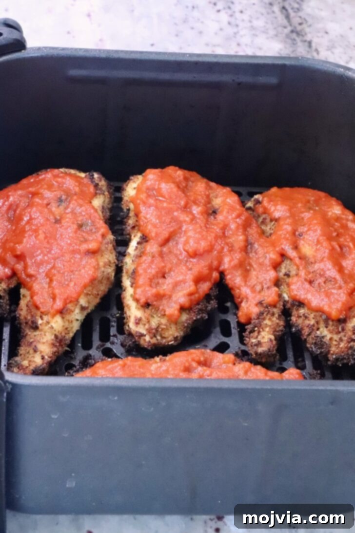 The Ultimate Air Fryer Chicken Parmesan 9 Crispy chicken breasts topped with marinara sauce, still in the air fryer basket, before adding cheese.