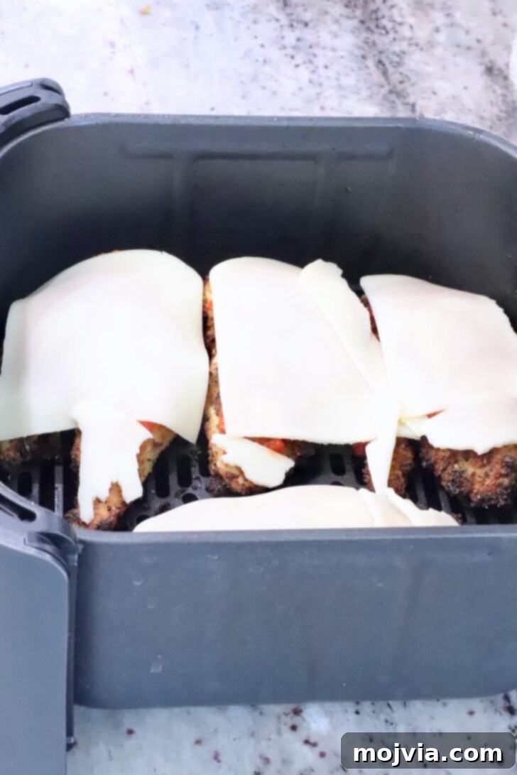 The Ultimate Air Fryer Chicken Parmesan 10 Mozzarella cheese slices melting beautifully over marinara-topped crispy chicken breasts in the air fryer basket.