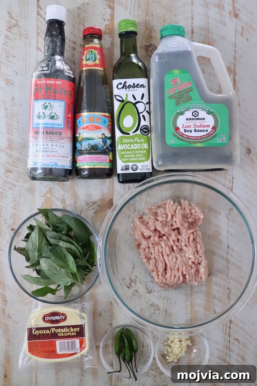 Thai Basil Chicken Dumplings: Flavorful Asian-Style Potstickers 5 Assorted cooking ingredients on a wooden surface, including fish sauce, oyster sauce, avocado oil, soy sauce, ground chicken, Thai basil, dumpling wrappers, chili peppers, and minced garlic.