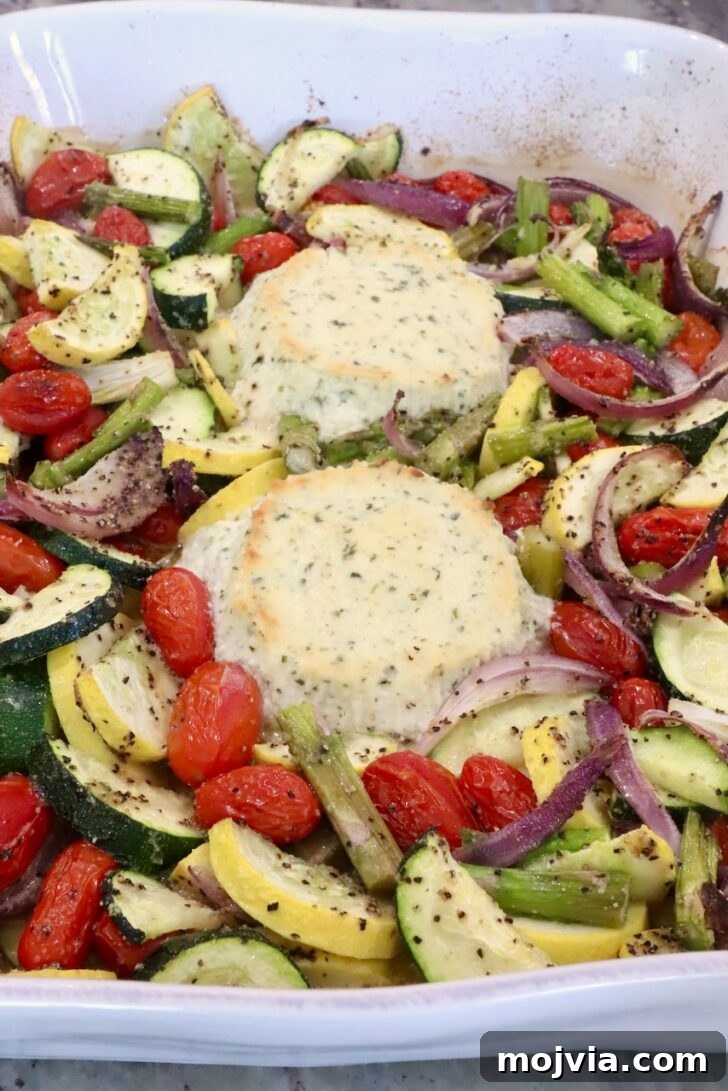 Creamy Boursin Pasta Primavera with Spring Vegetables 8 Roasted vegetables with two rounds of baked boursin cheese in a white baking dish. The veggies include zucchini, cherry tomatoes, asparagus, and red onions, seasoned with salt and pepper.