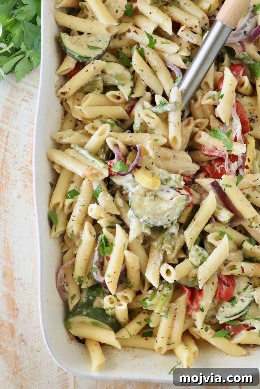 Creamy Boursin Pasta Primavera with Spring Vegetables 10 Creamy penne pasta in a white dish with zucchini, red onion, and tomatoes. Garnished with parsley.