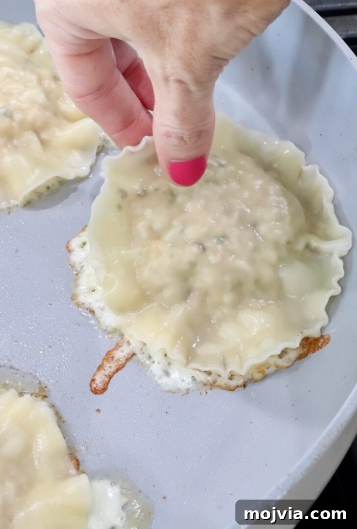hand placing a ravioli on top of a mozzarella cheese crust in a skillet