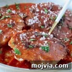 chicken ravioli with a mozzarella cheese crust in a bowl of marinara sauce with a fork, topped with fresh parsley and parmesan cheese