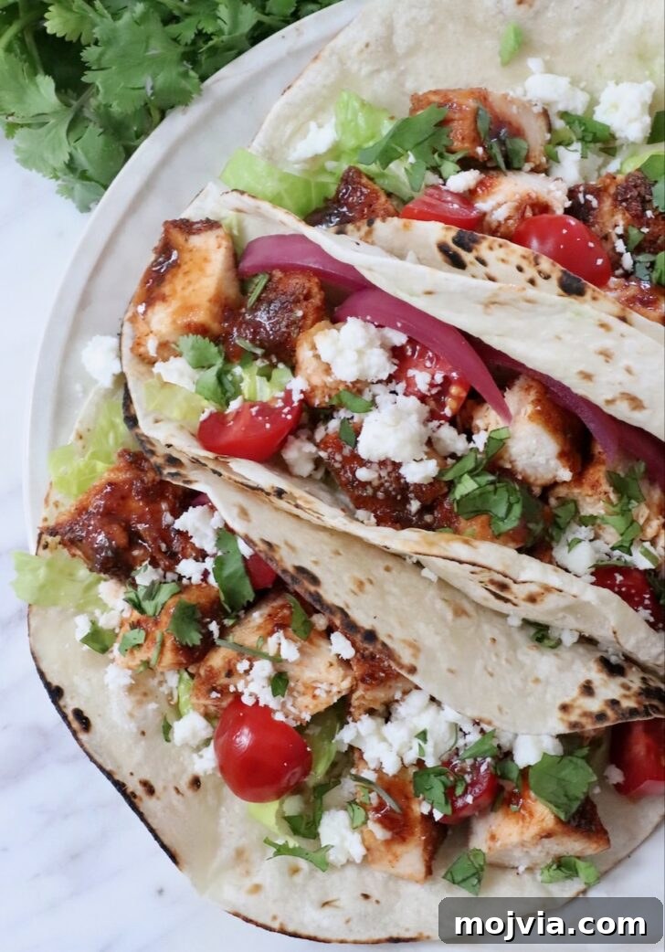 Chipotle Honey Chicken Tacos Made in the Air Fryer 11 air fryer chicken tacos topped with diced tomatoes, pickled onions, cilantro, lettuce, and crumbled cheese on lightly charred tortillas.