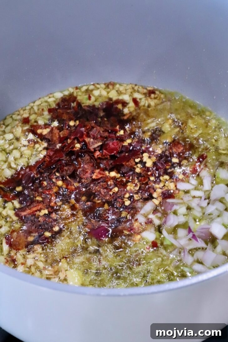 Calabrian Chili Crisp: Spicy Oil Recipe & Flavor Uses 9 pot filled with oil, garlic, shallots, and chopped dried chilies on the stove