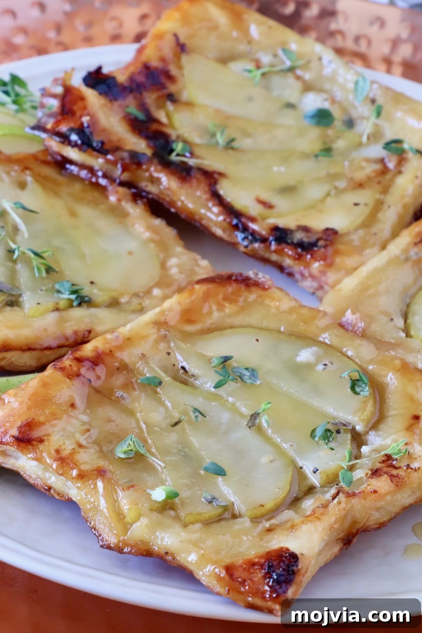 Gorgonzola and Pear Tart Recipe: Savory-Sweet Rustic Tart 2 Close-up of golden-brown puff pastry tarts topped with sliced pears and drizzled with honey, garnished with fresh thyme leaves.