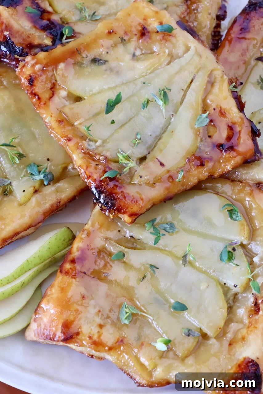 Gorgonzola and Pear Tart Recipe: Savory-Sweet Rustic Tart 15 Golden brown pear tarts topped with fresh thyme, placed on a white plate.