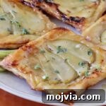 Gorgonzola and Pear Tart Recipe: Savory-Sweet Rustic Tart 16 Close-up of golden-brown puff pastry tarts topped with sliced pears and drizzled with honey, garnished with fresh thyme leaves.