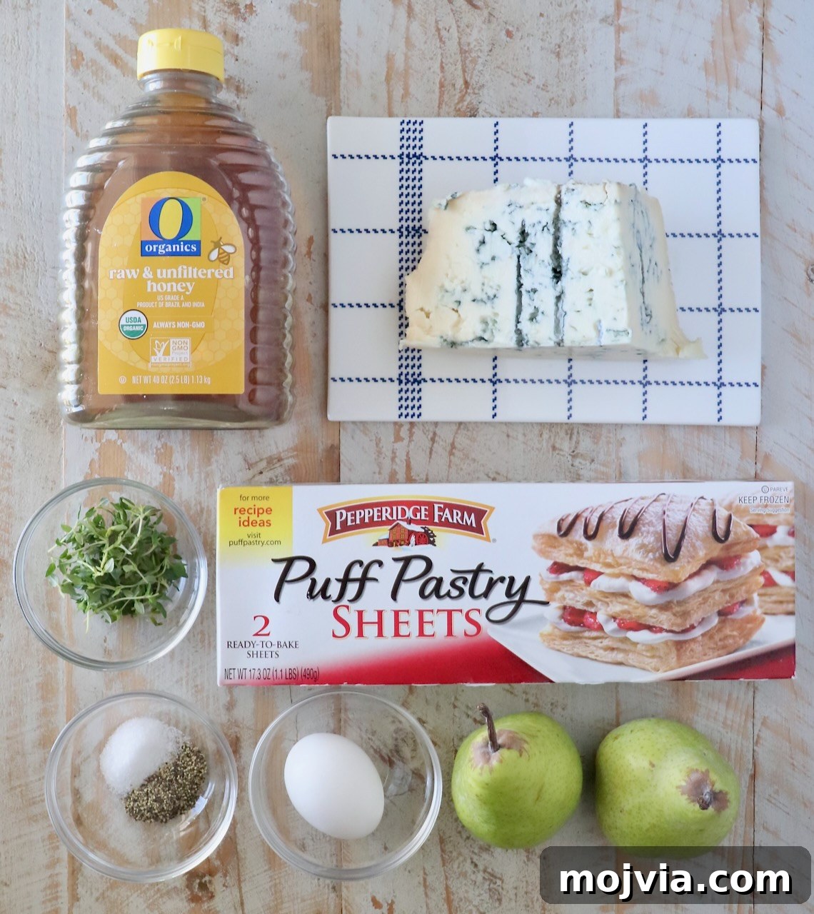 Gorgonzola and Pear Tart Recipe: Savory-Sweet Rustic Tart 5 Ingredients on a wooden table include honey, gorgonzola cheese, fresh thyme leaves, salt, pepper, an egg, pears, and puff pastry sheets.