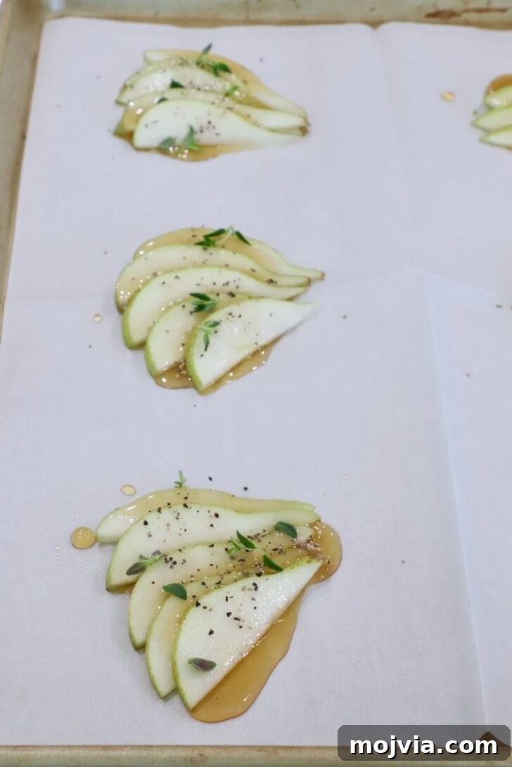 Gorgonzola and Pear Tart Recipe: Savory-Sweet Rustic Tart 9 sliced pears topped with honey, salt, pepper, and fresh thyme, on a sheet of parchment paper on a baking sheet