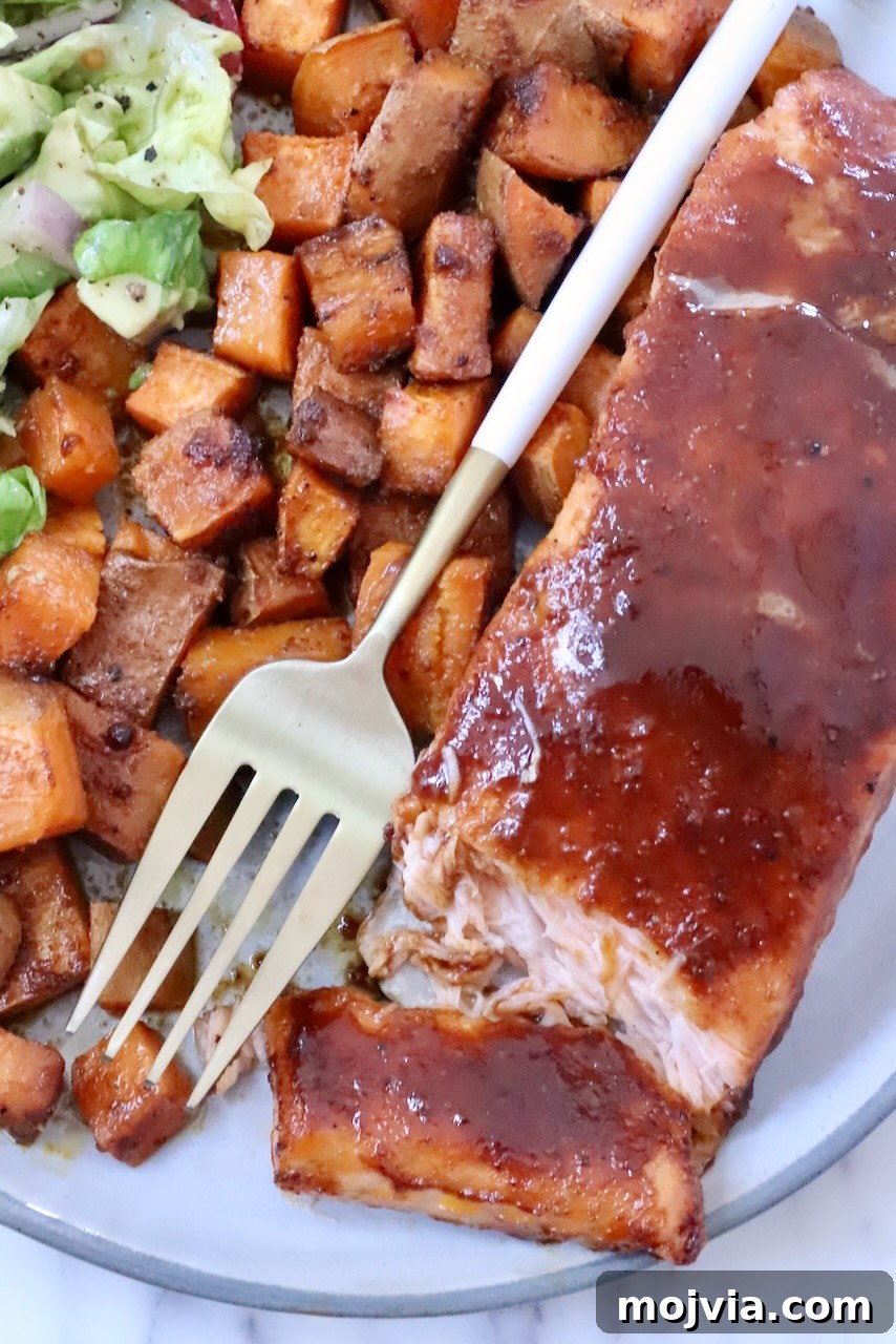 Grilled Salmon with Maple-Glazed Sweet Potatoes 2 A plate of glazed salmon fillet, accompanied by seasoned sweet potato cubes and a side salad. A gold fork rests on the plate.