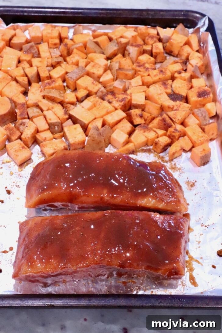 Grilled Salmon with Maple-Glazed Sweet Potatoes 7 diced seasoned sweet potatoes on a foil lined baking sheet with two salmon filets coated in bbq sauce