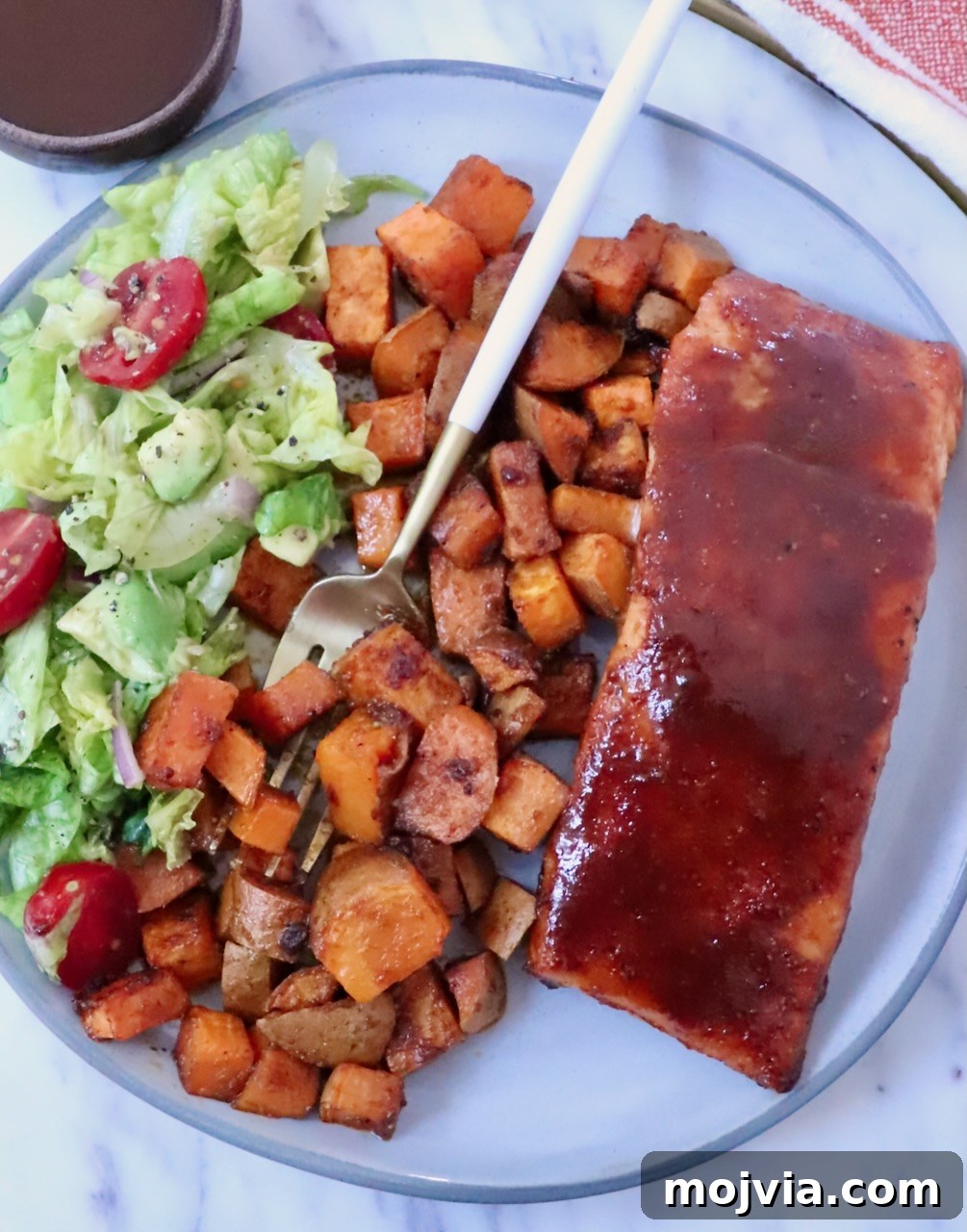 Grilled Salmon with Maple-Glazed Sweet Potatoes 8 bbq glazed salmon on a plate with roasted sweet potatoes, a side salad, and a fork
