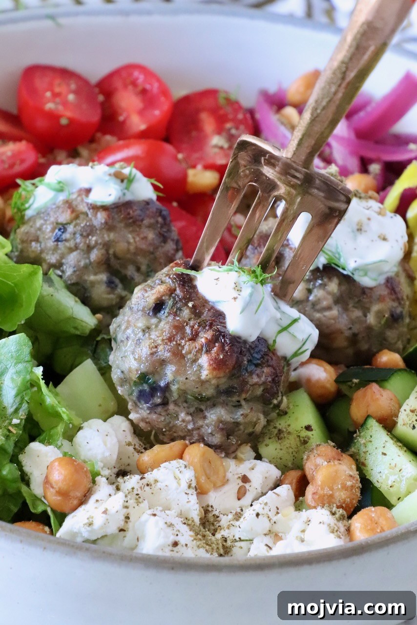 Greek Gyro Meatballs Recipe — Flavorful Mediterranean Meatballs 2 A bowl of vibrant Mediterranean salad with gyro meatballs topped with tzatziki sauce, sliced cherry tomatoes, cucumbers, crispy chickpeas, feta, and greens.