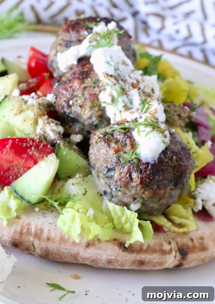 Greek Gyro Meatballs Recipe — Flavorful Mediterranean Meatballs 11 meatballs on top of pita bread on a plate, filled with lettuce, tomatoes, cucumber, and topped with creamy tzatziki sauce