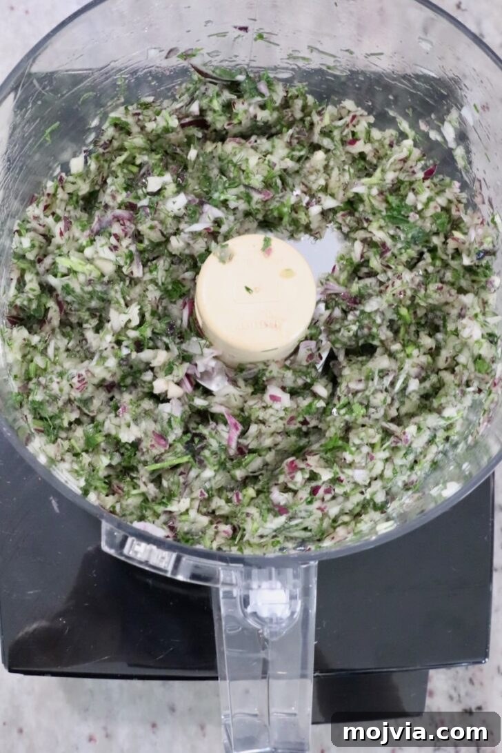 Greek Gyro Meatballs Recipe — Flavorful Mediterranean Meatballs 7 Chopped herbs and vegetables, including red onion and parsley, in a food processor bowl.