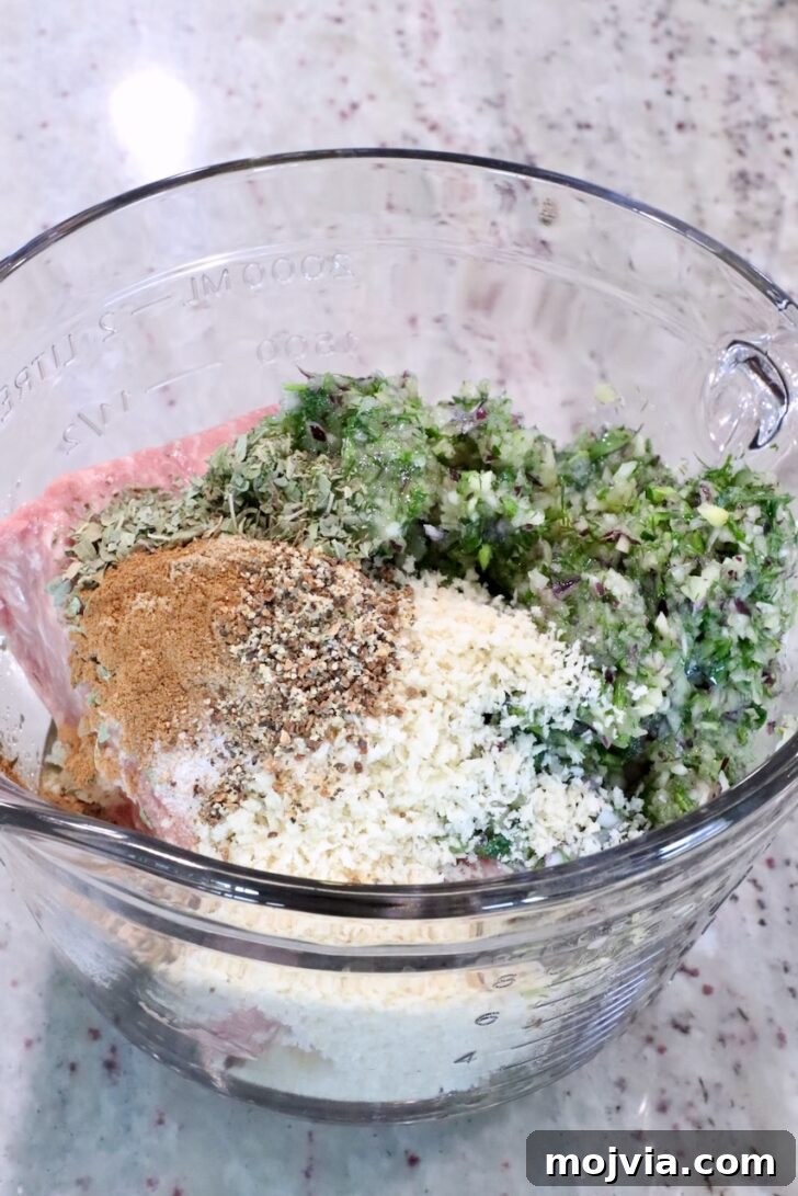 Greek Gyro Meatballs Recipe — Flavorful Mediterranean Meatballs 8 Glass bowl with minced meat, breadcrumbs, chopped herbs, and spices on a marble countertop.