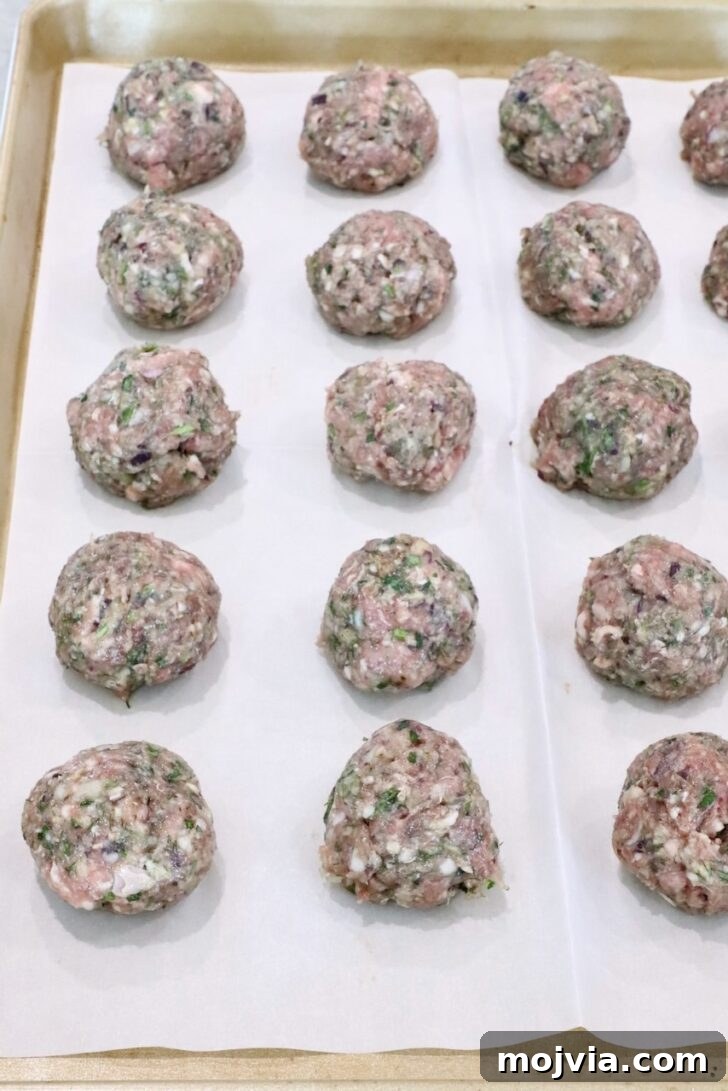 Greek Gyro Meatballs Recipe — Flavorful Mediterranean Meatballs 9 Raw meatballs arranged in rows on a parchment-lined baking sheet.