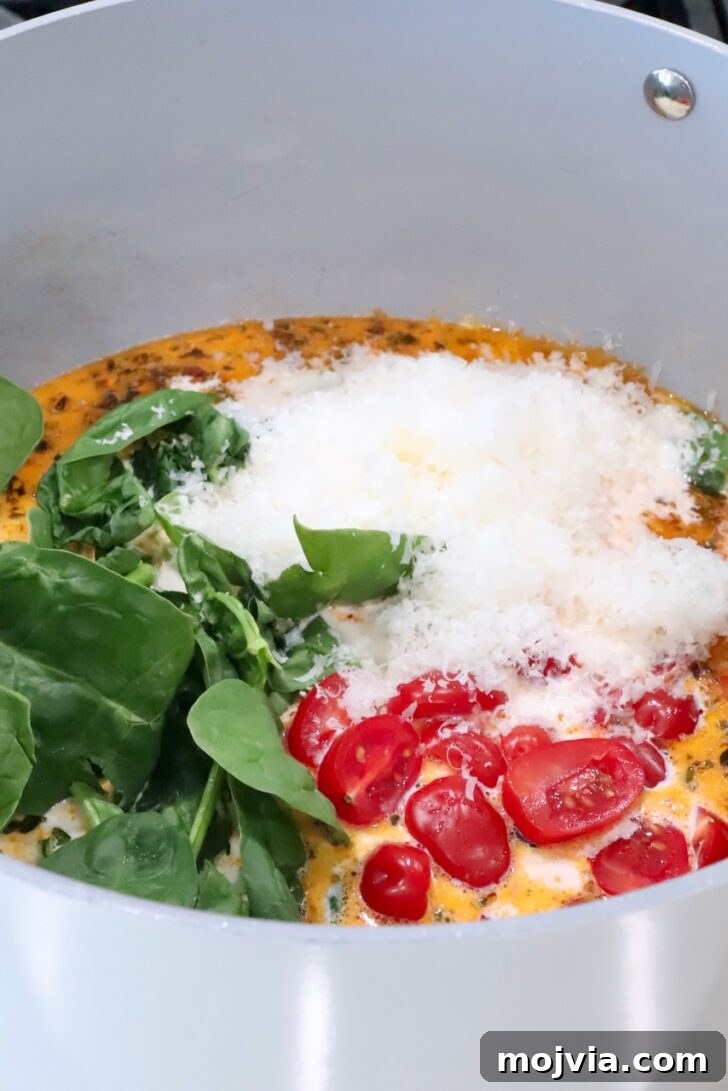 Creamy Tuscan Chicken Pasta Recipe with Sun-Dried Tomatoes 10 creamy sauce topped with diced cherry tomatoes, grated parmesan cheese and fresh spinach in a sauce pan