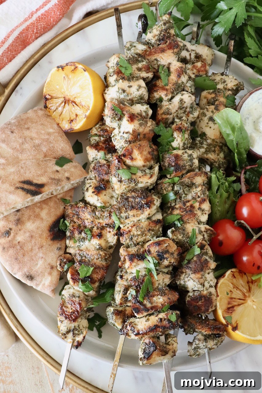 Authentic Greek Souvlaki Recipe: How to Make Classic Meat Skewers 2 chicken souvlaki on skewers stacked up on a plate next to grilled pita bread, lemons and tomatoes