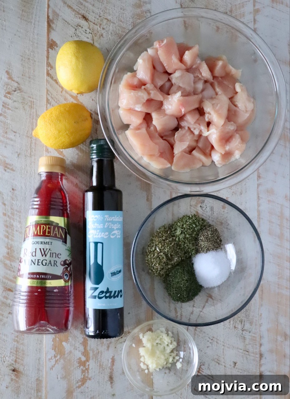Authentic Greek Souvlaki Recipe: How to Make Classic Meat Skewers 5 ingredients for souvlaki on a white wood board including a bowl of cubed chicken, olive oil, lemons, red wine vinegar, minced garlic, and spices
