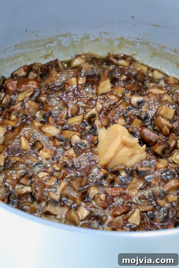 Savory Mushroom Jam Recipe for Spreading and Cooking 11 mushroom jam in a pot on the stove with a scoop of white miso paste