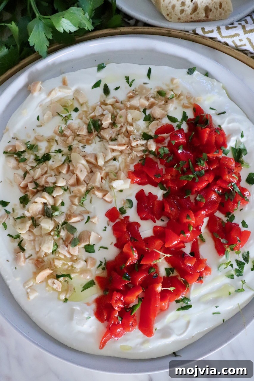 Whipped Goat Cheese Dip Recipe for Entertaining and Snacks 2 whipped goat cheese dip on a rimmed plate topped with chopped almonds, roasted red peppers and fresh herbs