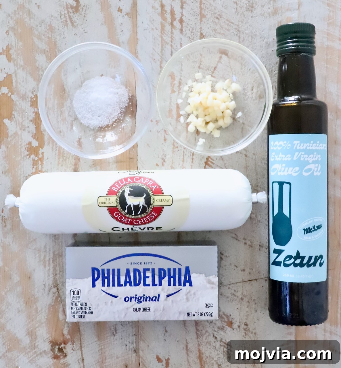 Whipped Goat Cheese Dip Recipe for Entertaining and Snacks 5 ingredients for goat cheese dip on a white wood board including olive oil, cream cheese, goat cheese, minced garlic and salt