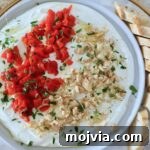 Whipped Goat Cheese Dip Recipe for Entertaining and Snacks 10 creamy goat cheese dip on a plate topped with chopped almonds, roasted red peppers, and fresh parsley, with a sliced baguette on the side