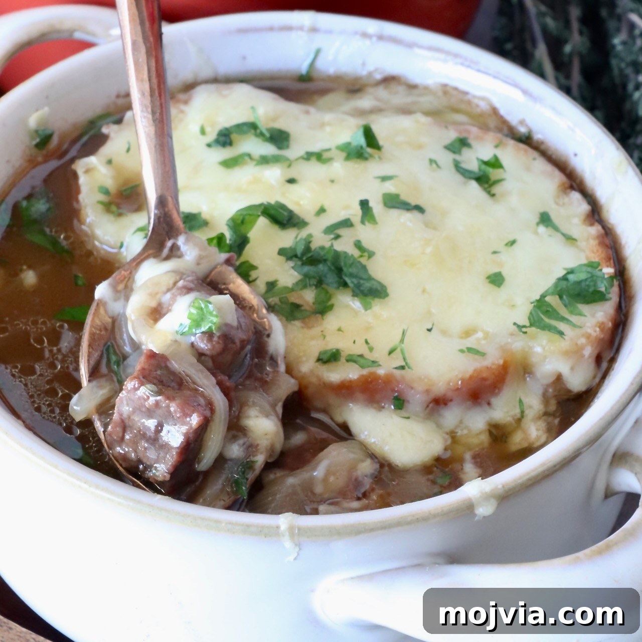 A bowl of French onion beef stew topped with melted cheese and herbs.