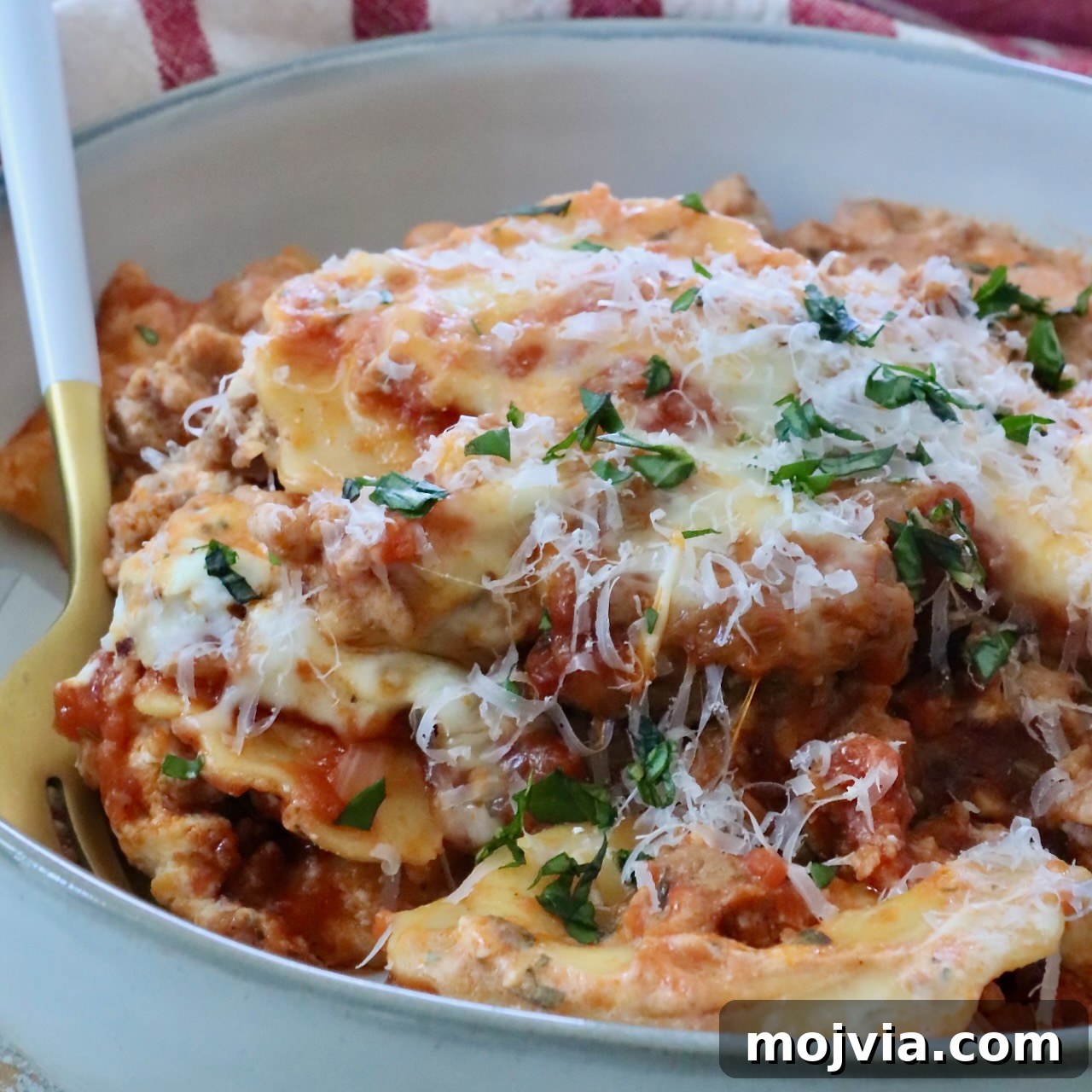 Close-up of a bowl of baked ravioli with melted cheese, garnished with fresh herbs