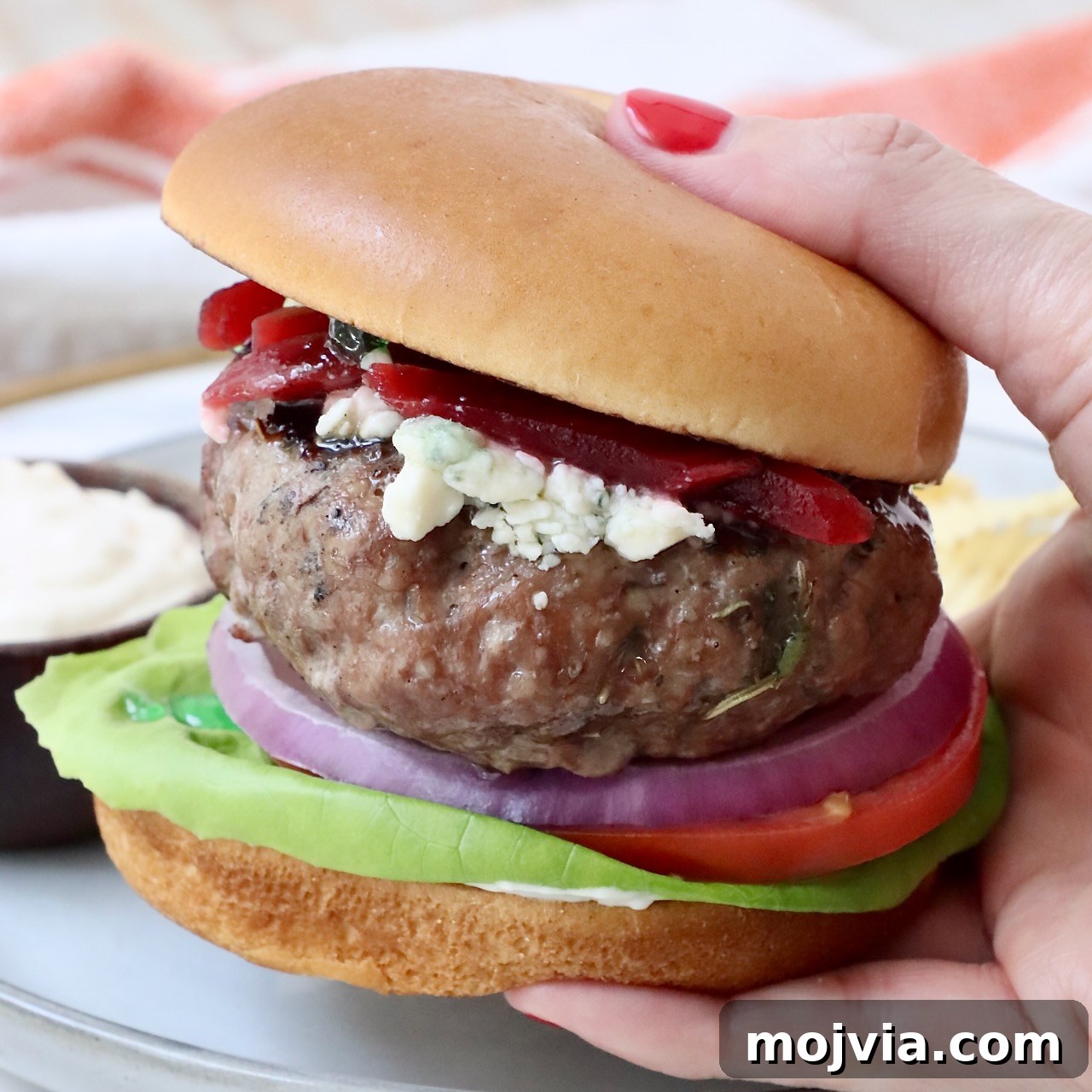 hand holding a lamb burger on a bun over a plate