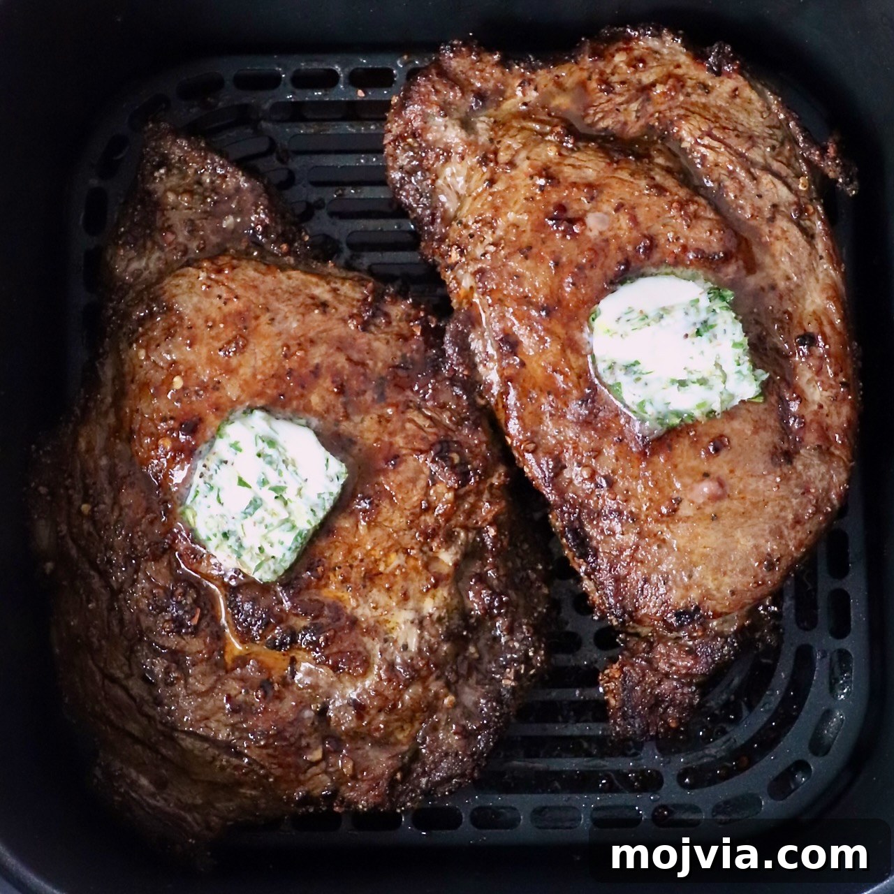 cooked ribeye steaks in an air fryer basket topped with herb compound butter