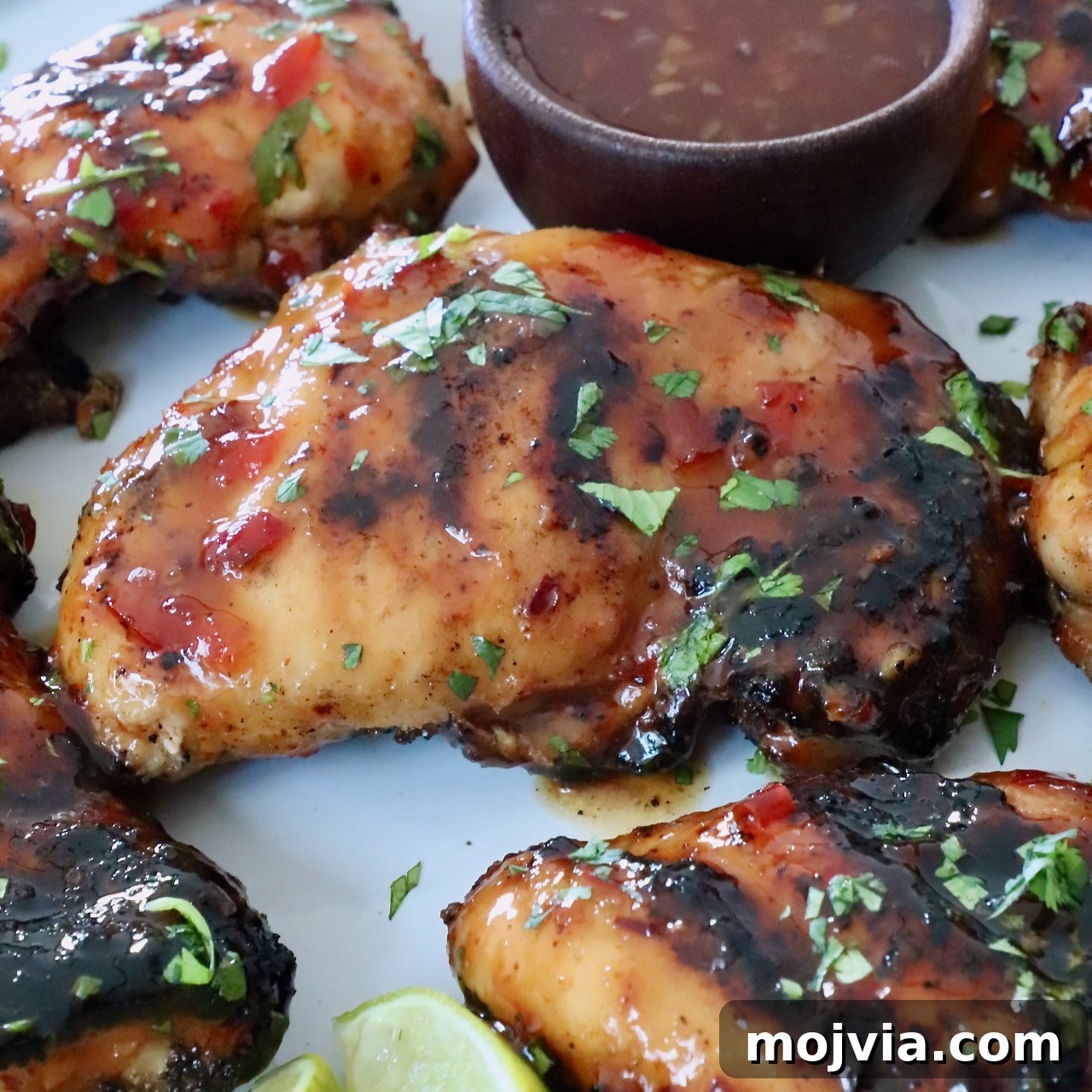 Grilled Thai glazed chicken thighs topped with fresh herbs on a white plate.