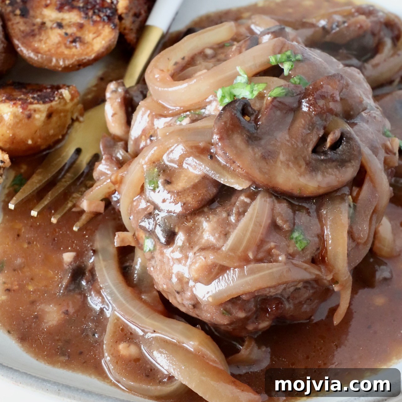 cooked chopped steak on a plate, covered with cooked, sliced onions and mushrooms and gravy