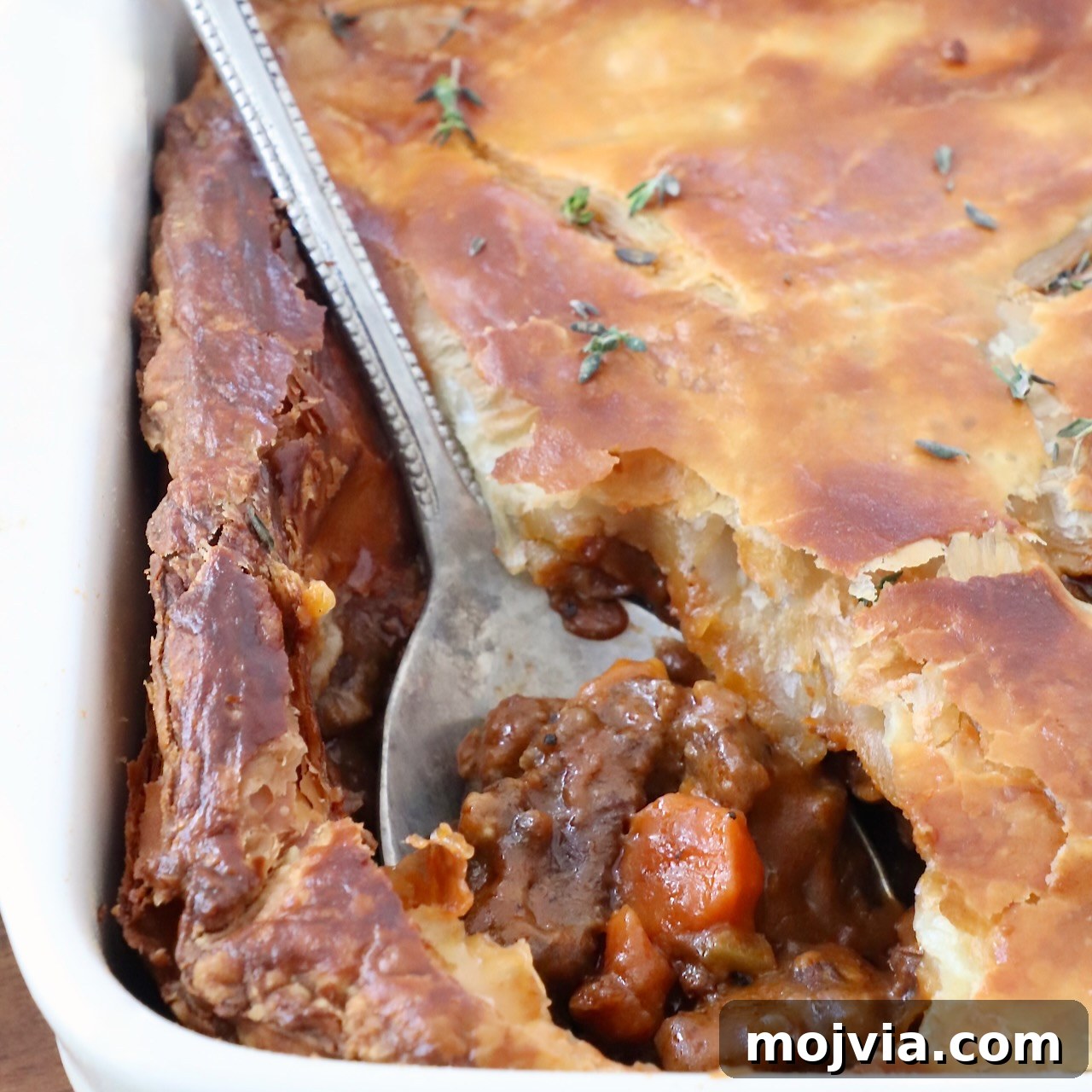 serving spoon in a beef pot pie in a baking dish