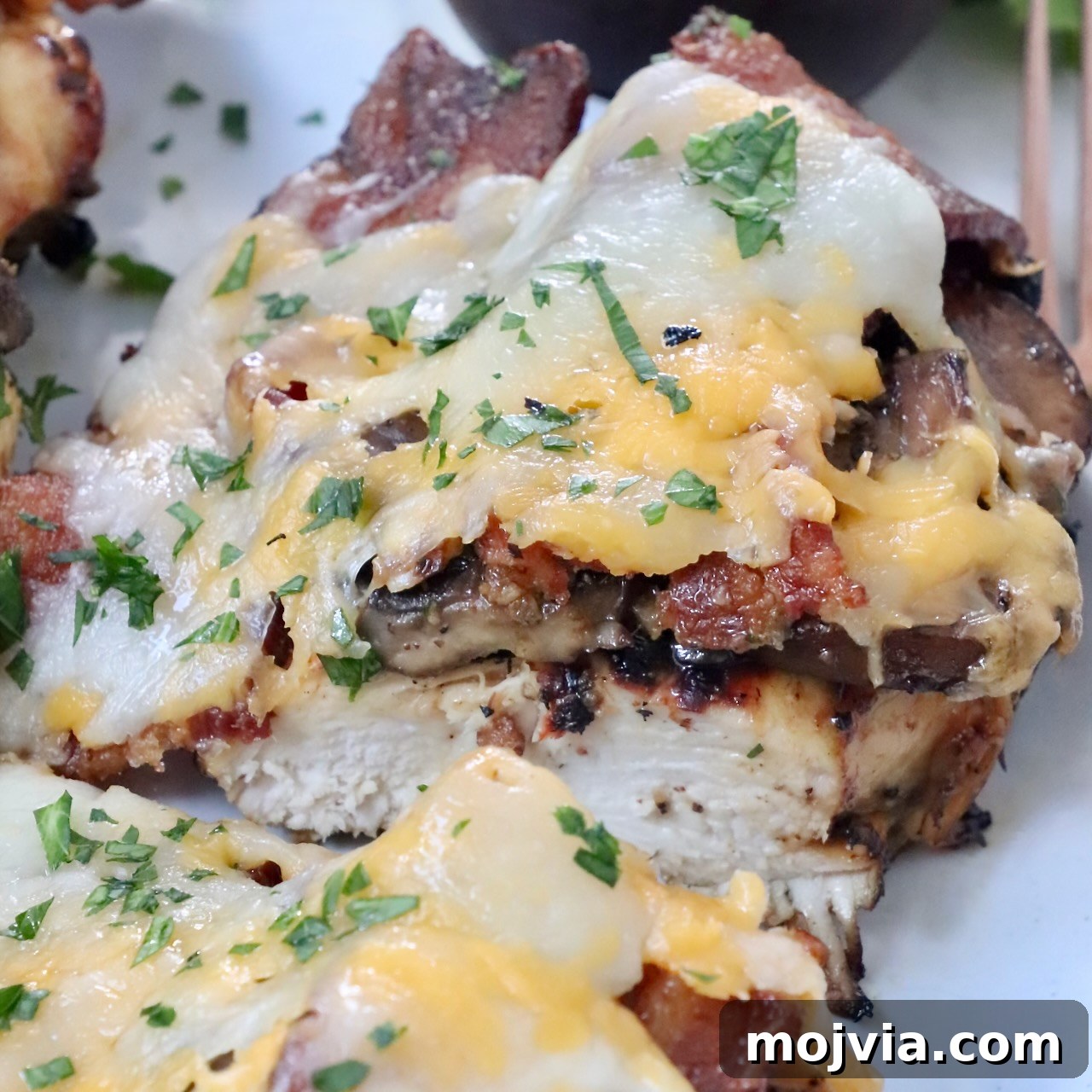 grilled chicken topped with bacon and cheese sliced in half on plate