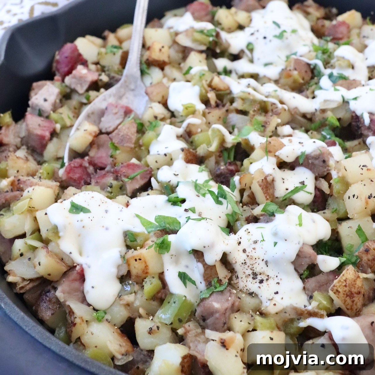 steak and potato hash in skillet topped with cheese sauce
