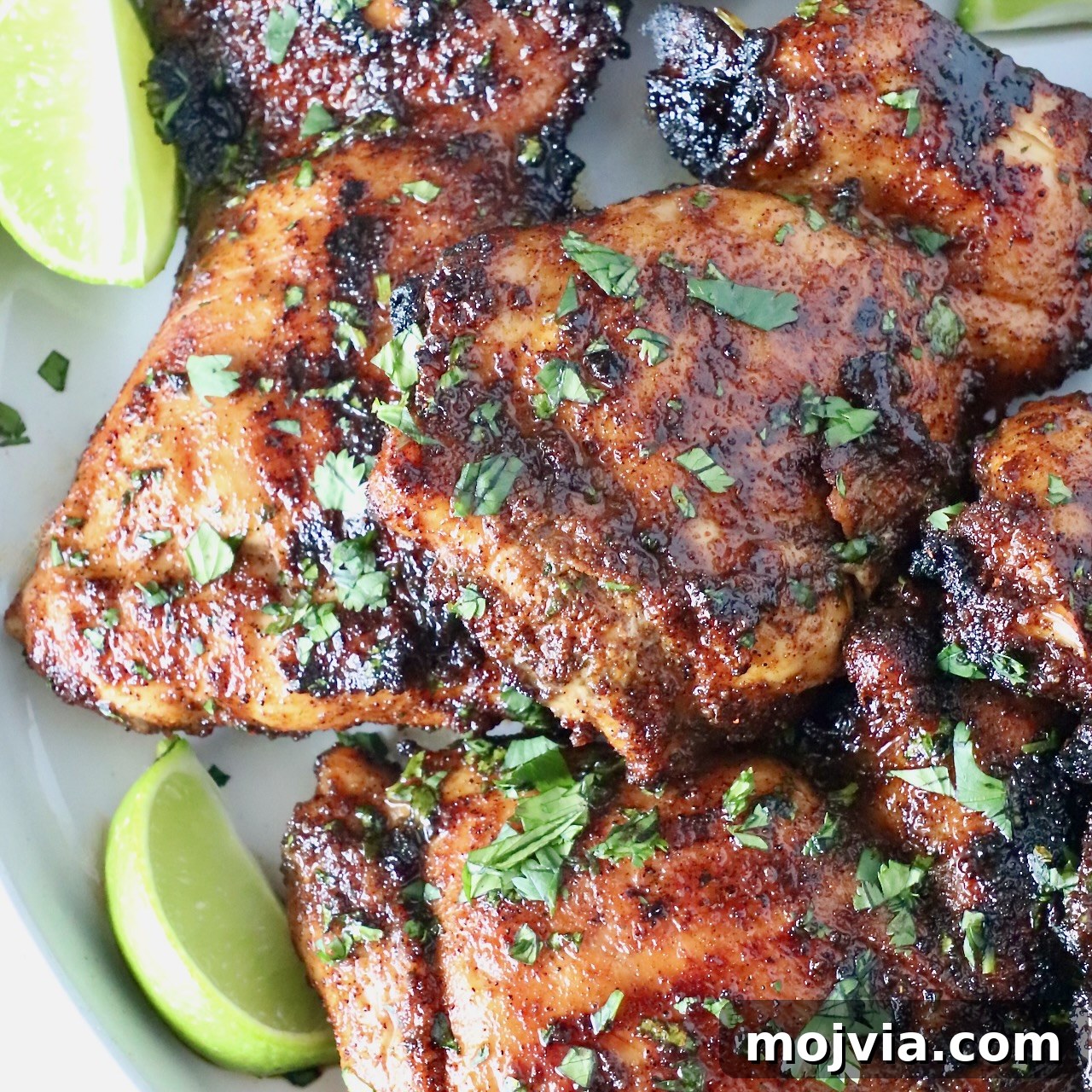grilled chicken thighs stacked up on a plate with fresh cilantro and lime wedges