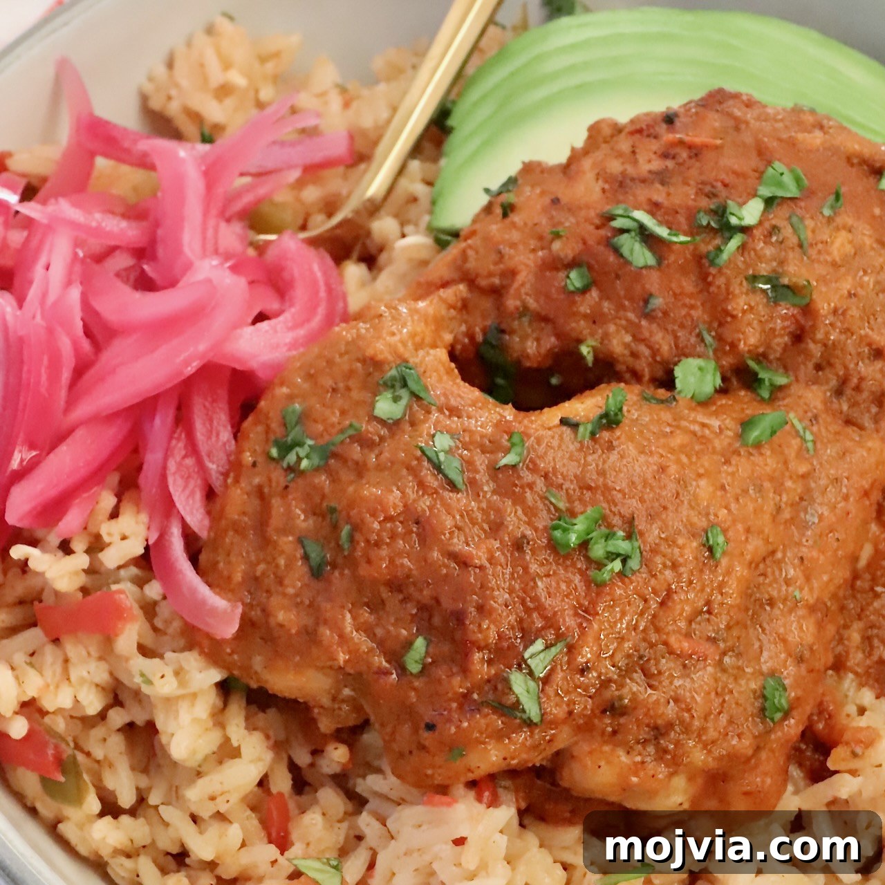 cooked chicken covered in adobo sauce on top of rice in a bowl with avocado and pickled onions