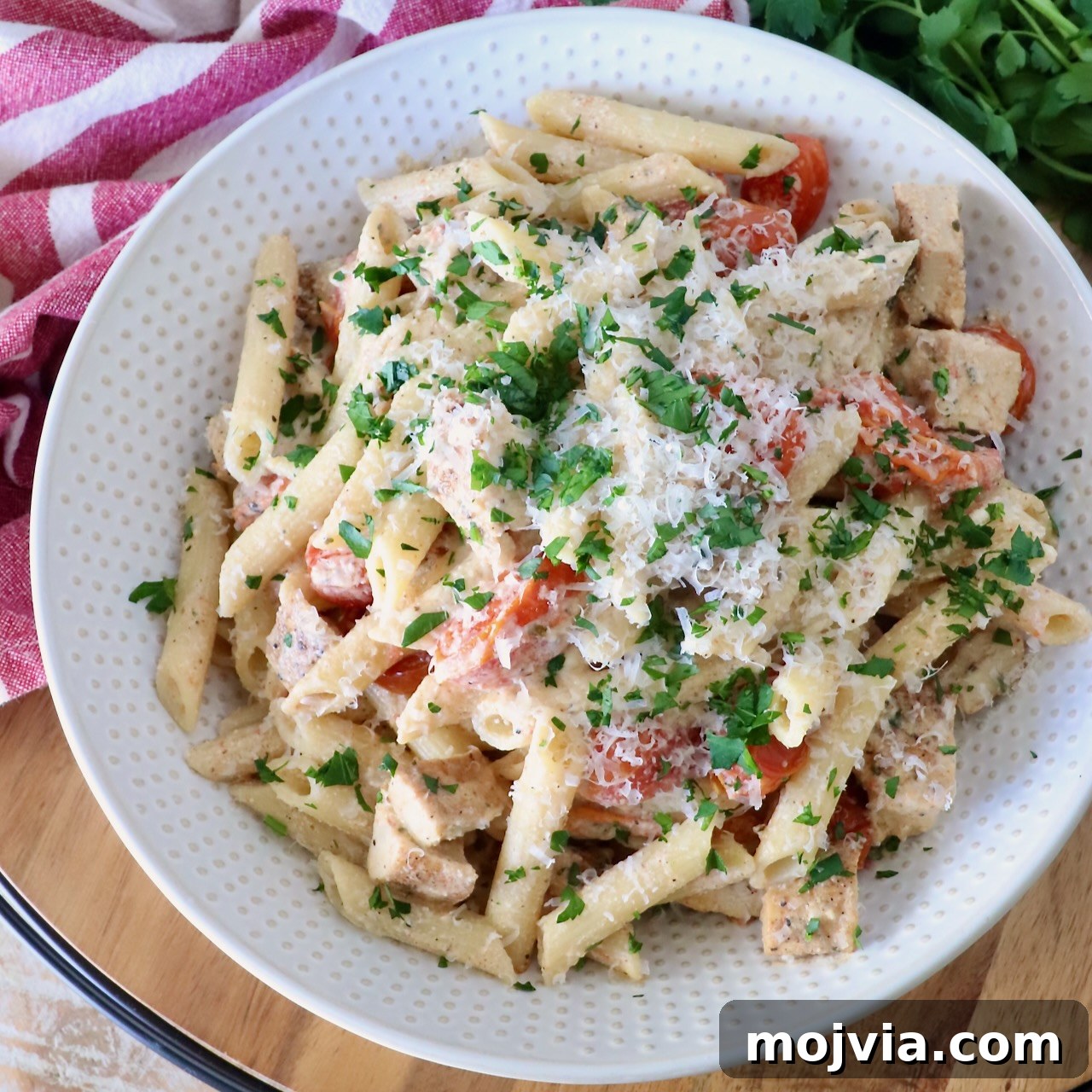 A white bowl of creamy penne pasta with diced chicken, cherry tomatoes, and parsley