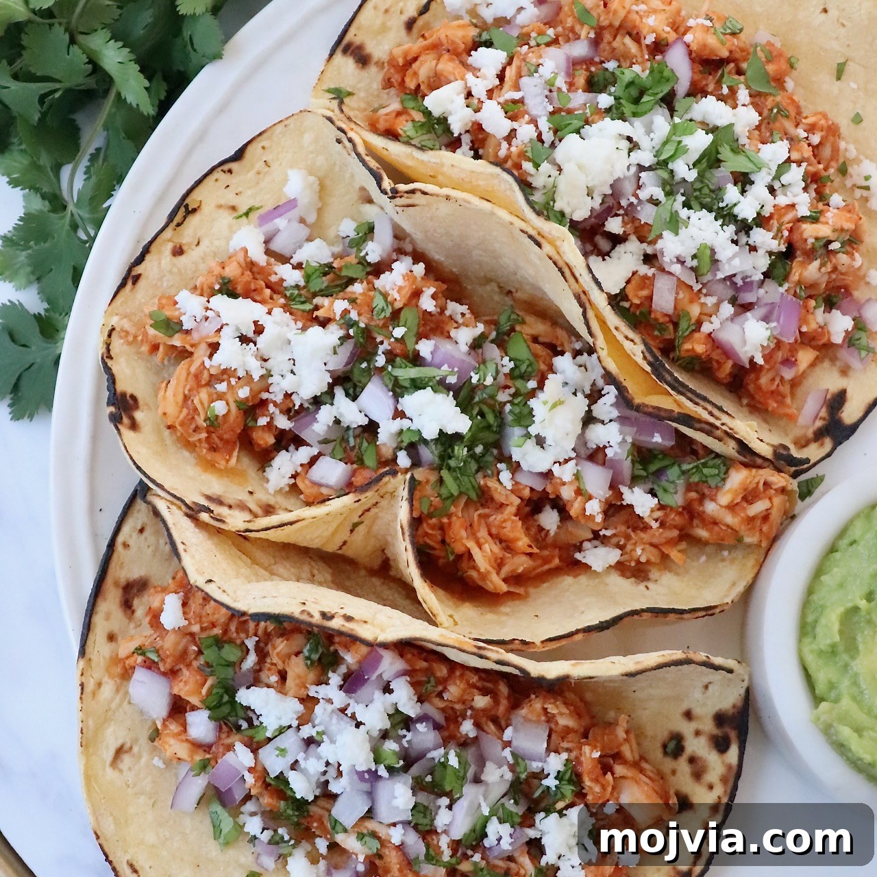 tacos on plate filled with cooked, shredded chicken, cheese, diced onions and cilantro